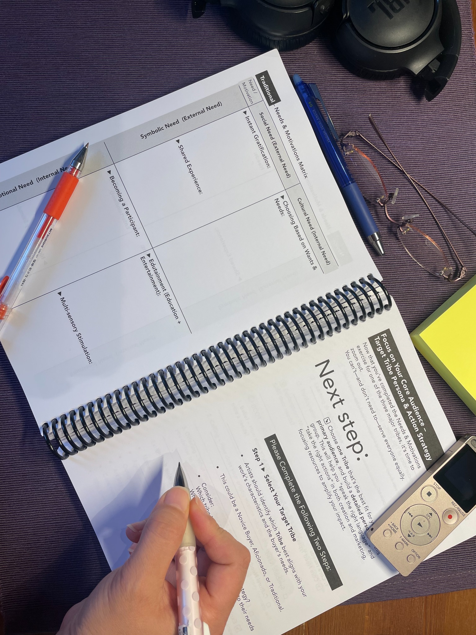 An open workbook being used at a desk with pens and notes
